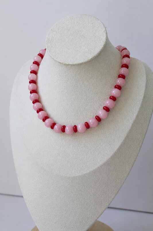 Pink and red handcrafted beaded necklace displayed on a jewelry bust.