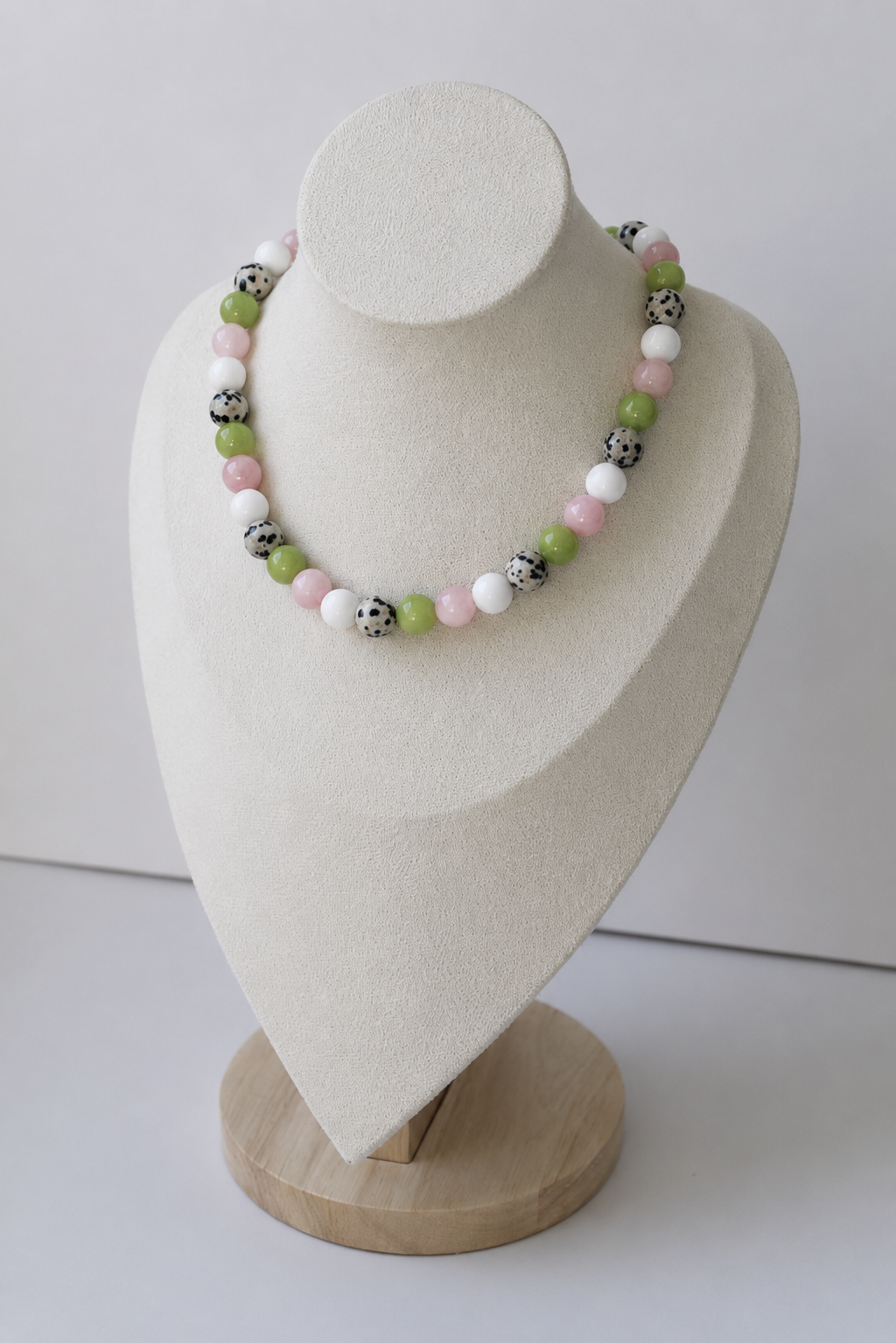 Colorful beaded necklace featuring blush pink, white, green, and dalmatian-inspired beads displayed on a jewelry bust.