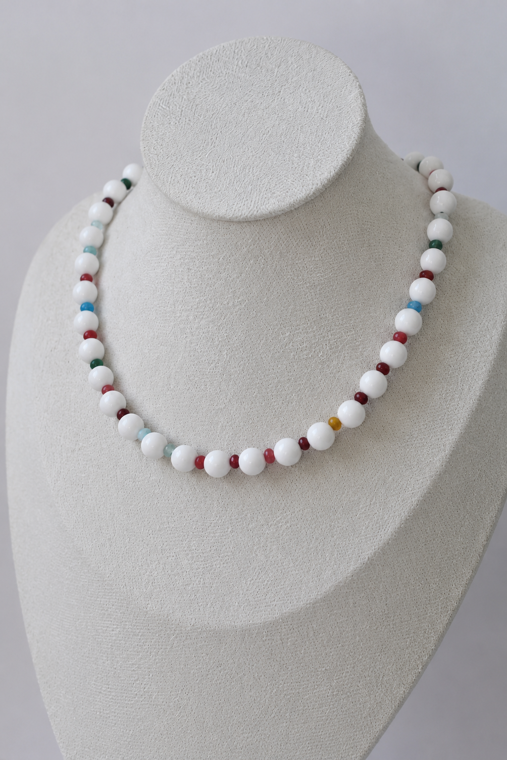 White beaded necklace with colorful accent beads displayed on a jewelry bust.