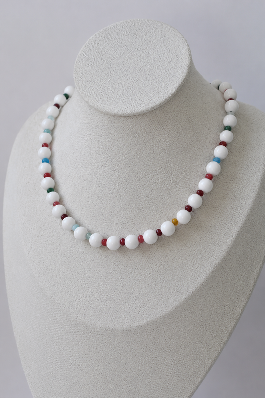 White beaded necklace with colorful accent beads displayed on a jewelry bust.