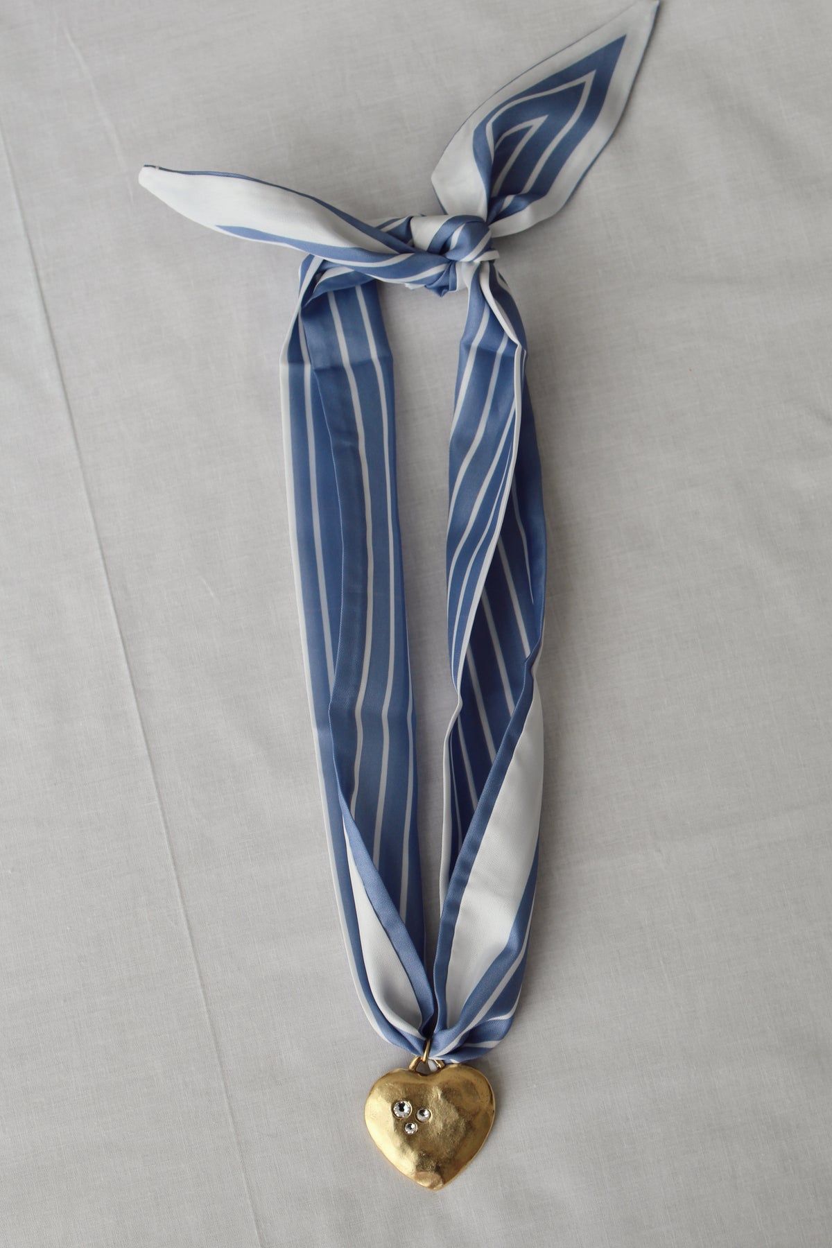 Gold heart pendant with crystal details on blue striped scarf necklace