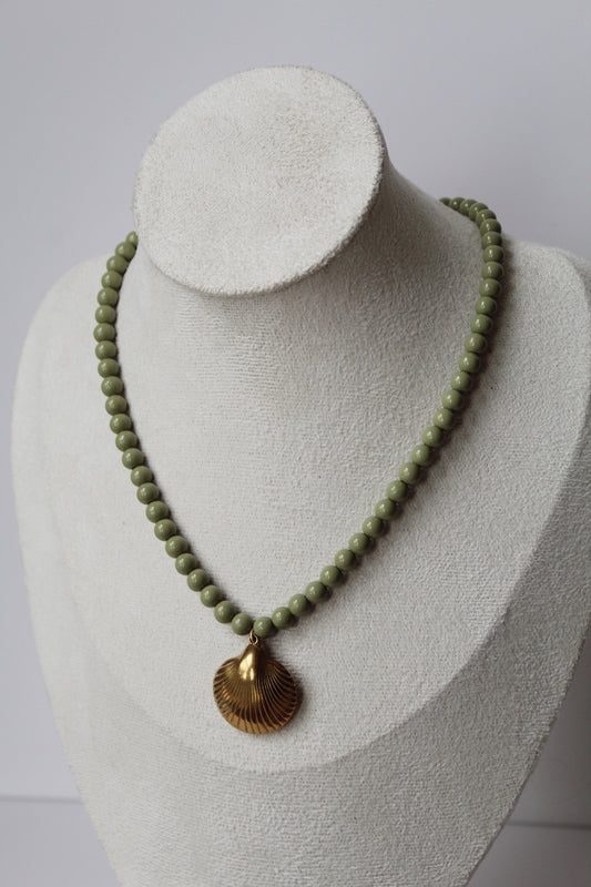 Sage green beaded necklace with a gold shell pendant displayed on a jewelry bust.