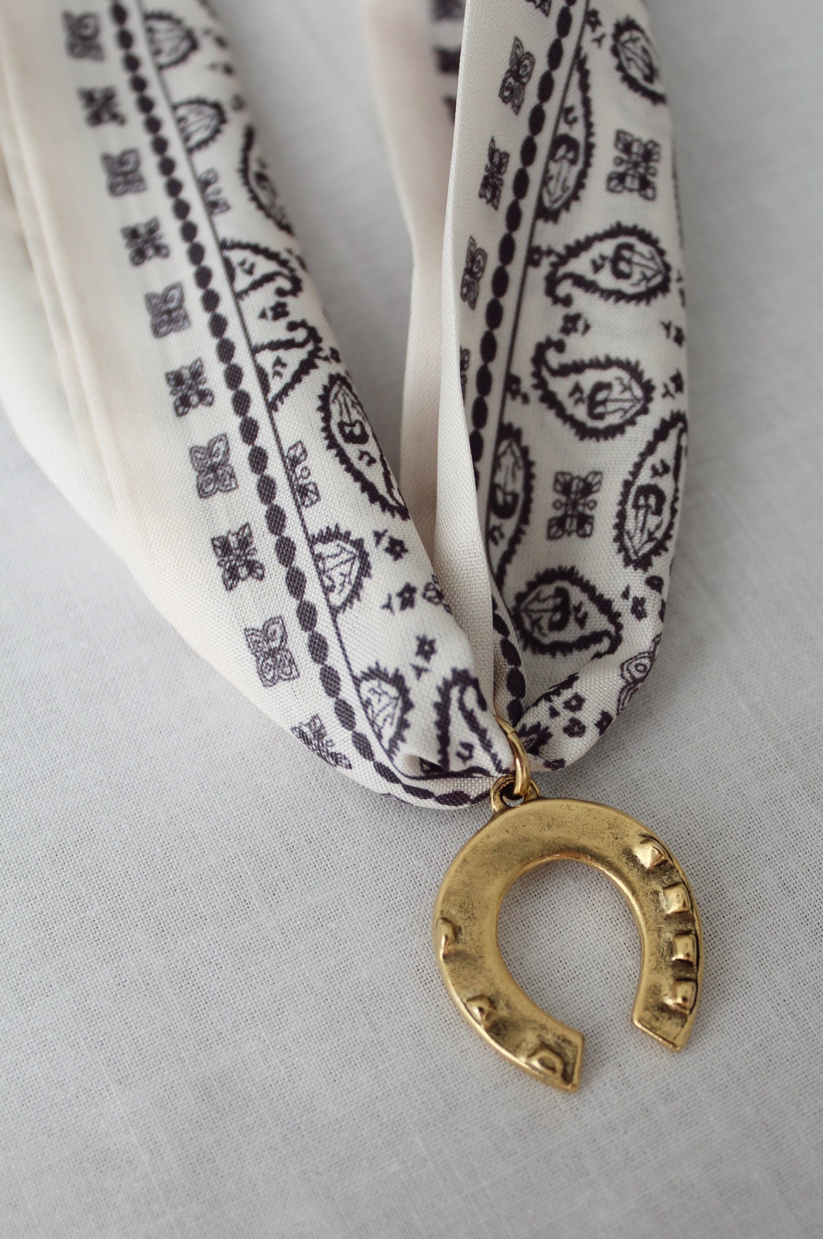 Vintage-inspired gold horseshoe pendant on ivory and black scarf necklace
