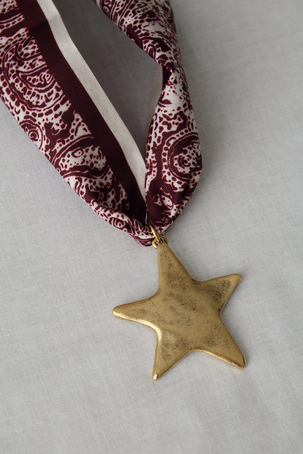 Gold star pendant on burgundy and cream paisley scarf necklace