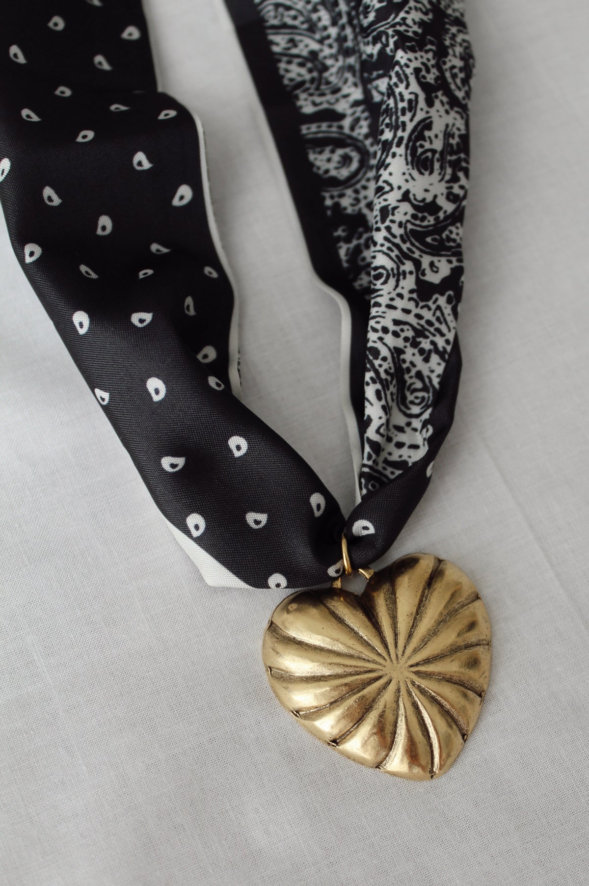Sculptural gold heart pendant on black and white paisley scarf necklace