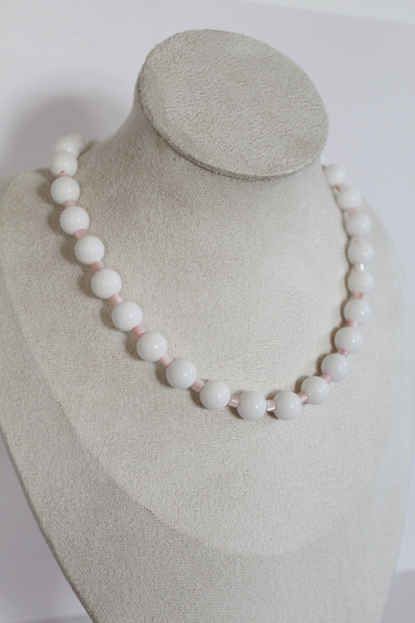 Handcrafted white acrylic beaded necklace with blush pink spacer beads displayed on a jewelry bust.