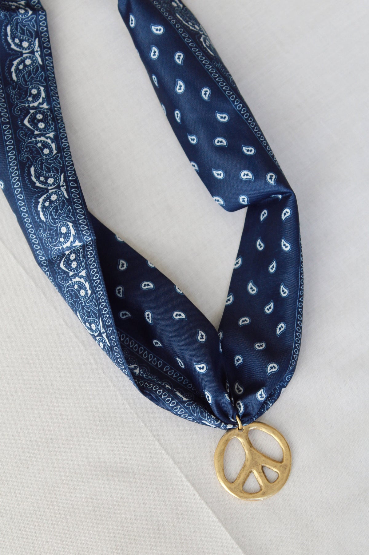 Gold peace sign pendant on navy and white paisley scarf necklace