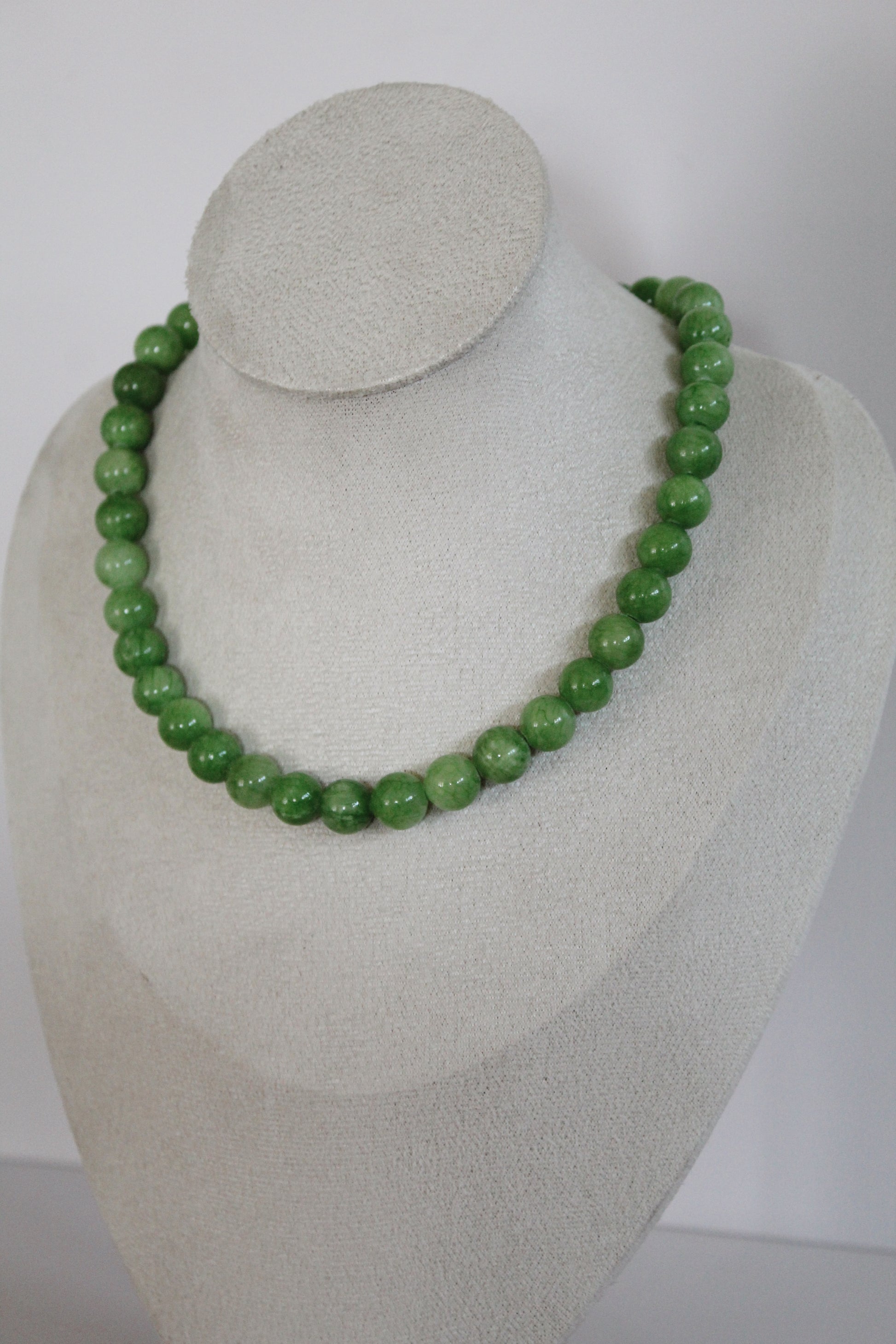 Handcrafted marbled green acrylic beaded necklace displayed on a jewelry bust.
