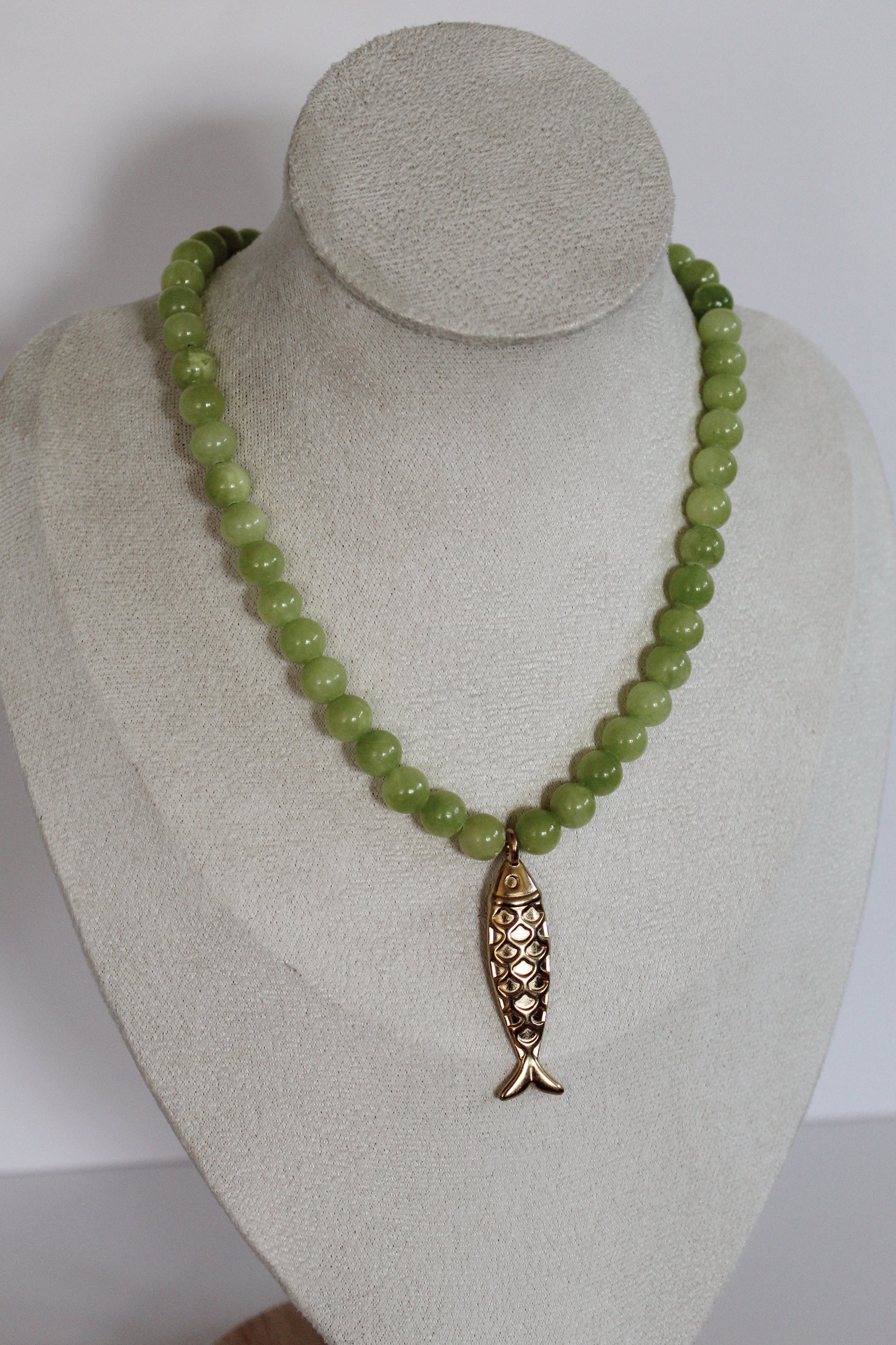 Handcrafted lime green acrylic beaded necklace featuring a vintage-inspired gold fish charm displayed on a jewelry bust.