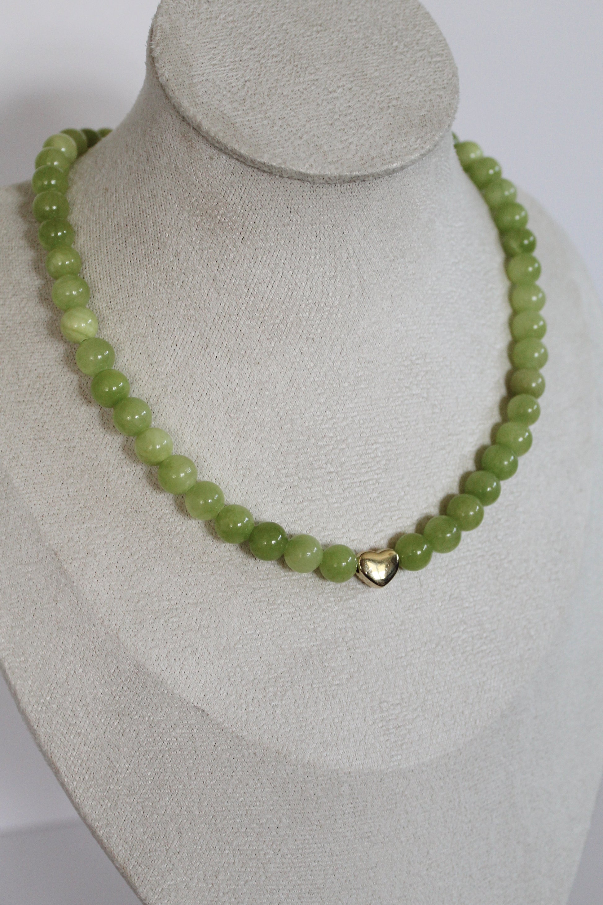 Handcrafted lime green acrylic beaded necklace with a gold heart accent displayed on a jewelry bust.