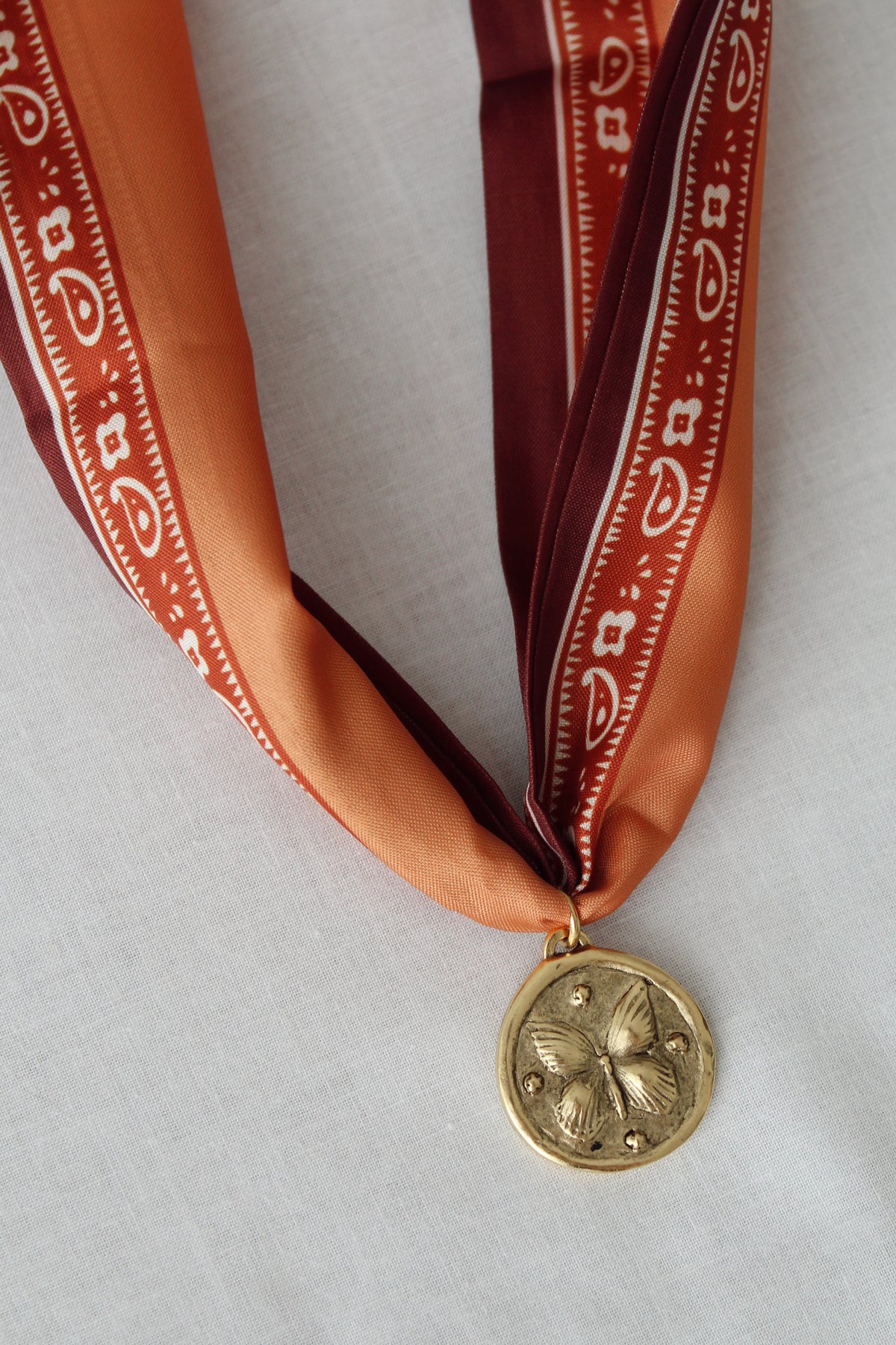 Vintage-inspired gold flower pendant on rust printed scarf necklace
