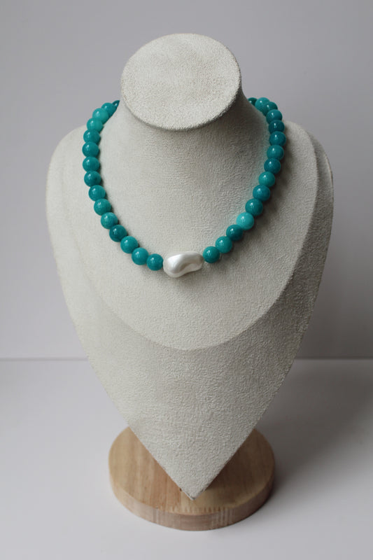 Turquoise beaded necklace with a pearl centerpiece displayed on a jewelry bust.