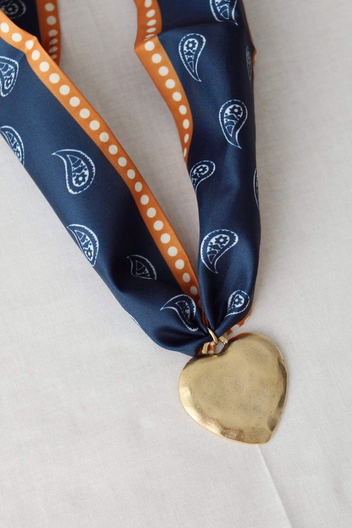 Oversized gold heart pendant on navy and burnt orange scarf necklace